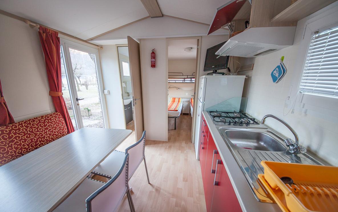 Interno di una casa mobile con cucina, tavolo e camera da letto.